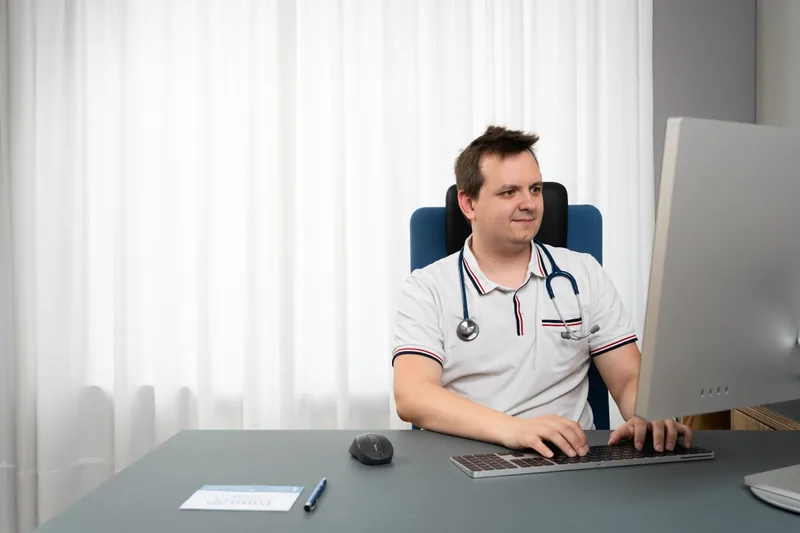 Helmut Steinbrecher wearing a stethoscope at his computer in his medical practice